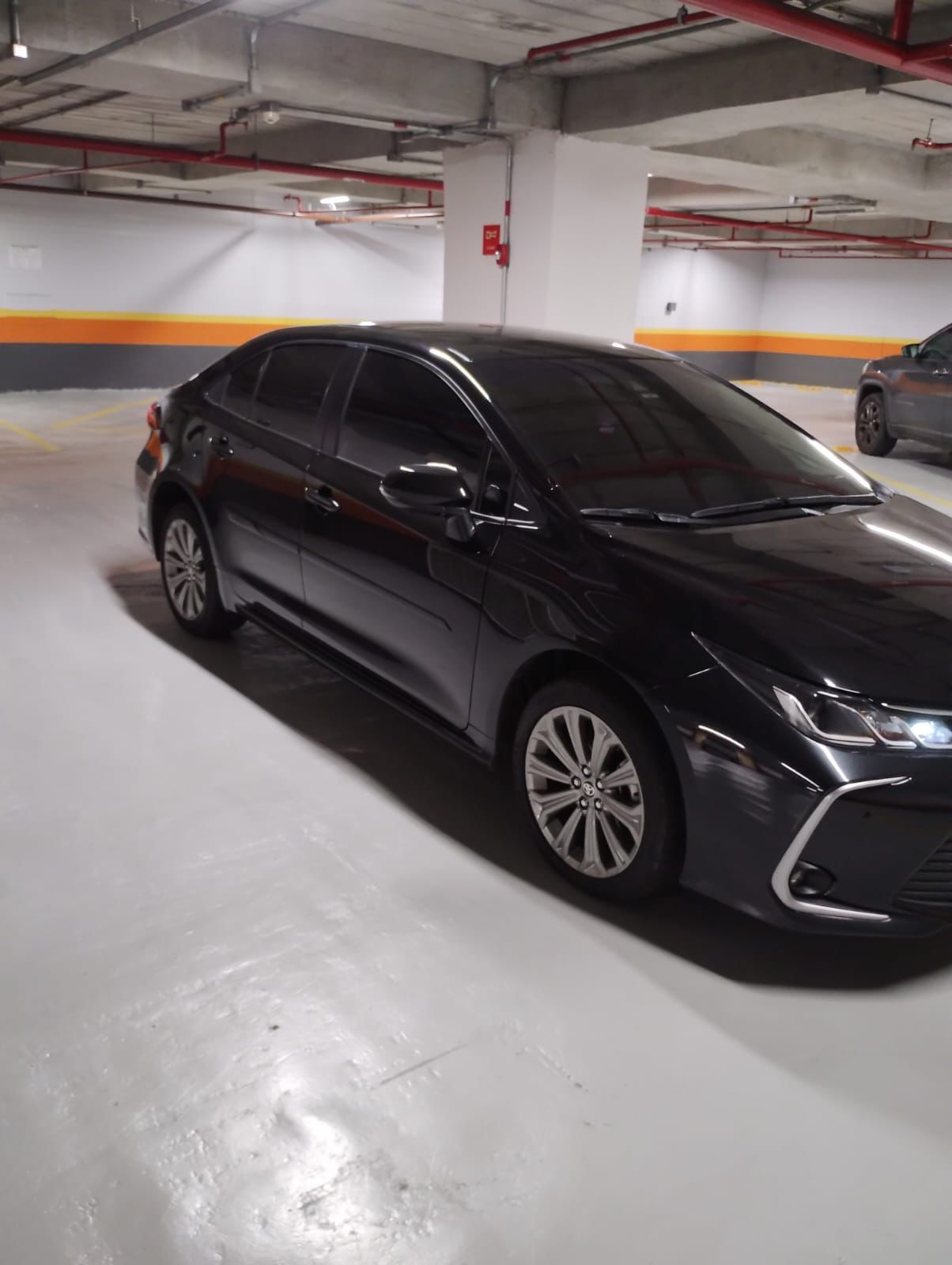 Carro preto Seventy Trans estacionado em garagem coberta com paredes brancas e detalhes amarelos e pretos.