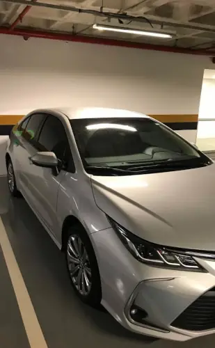 Carro sedan Corola prateado da Seventy Trans Log estacionado em uma garagem coberta